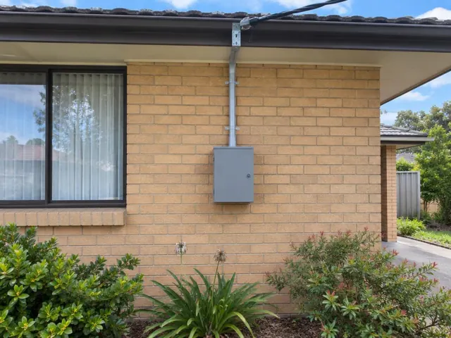 Overhead service cable and point-of-attachment bracket above a brick house wall with meter box in Empire Bay